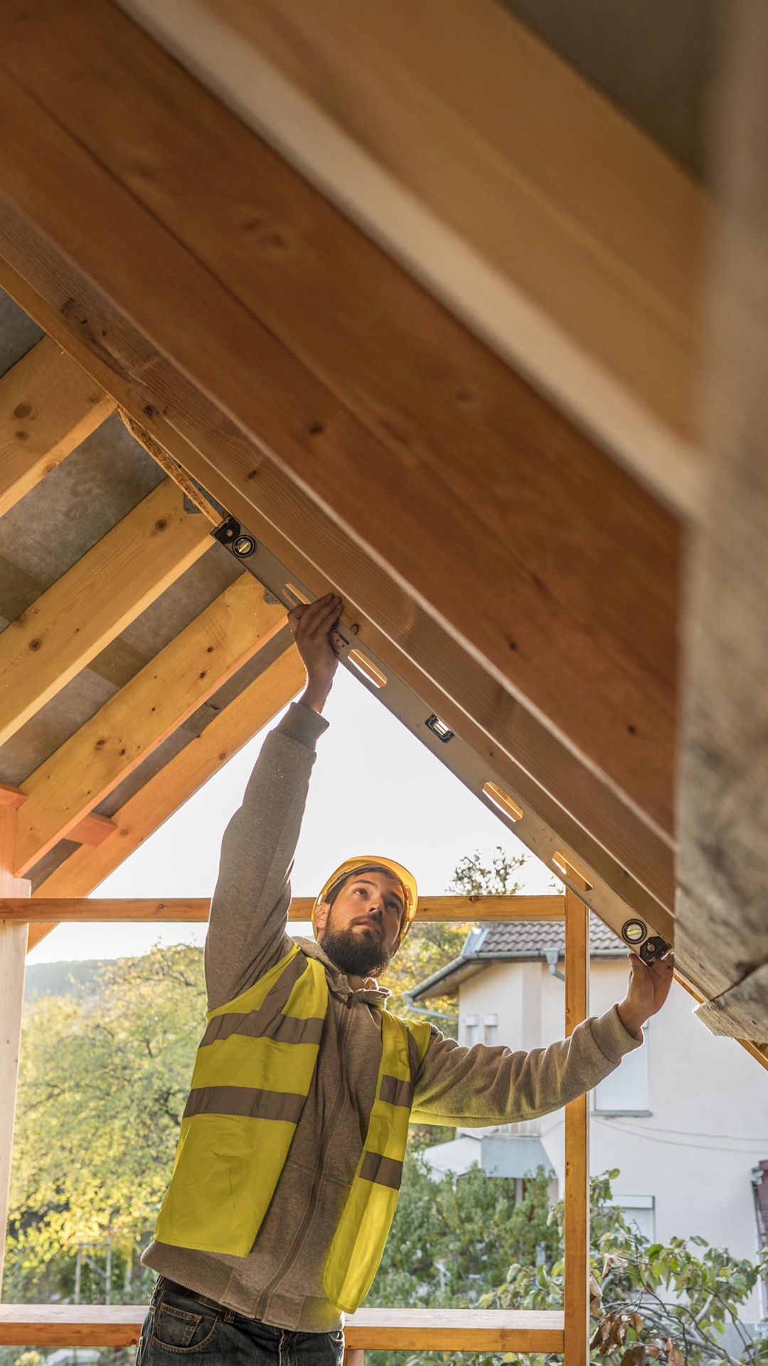 Charpentier vérifiant l’inclinaison d’une poutre en bois sur le chantier d’une maison individuelle
